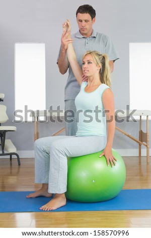 Physiotherapist correcting patient sitting on exercise ball in bright room