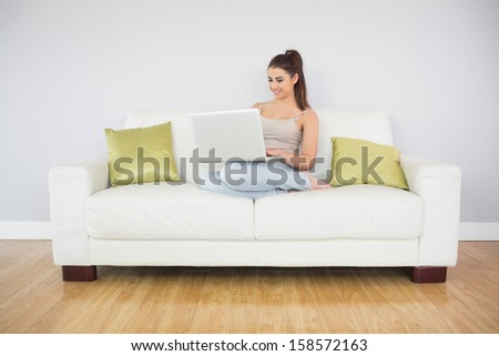 Happy woman using her notebook while sitting on a white couch