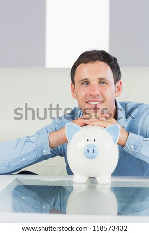 Happy casual man resting head on piggy bank in bright living room