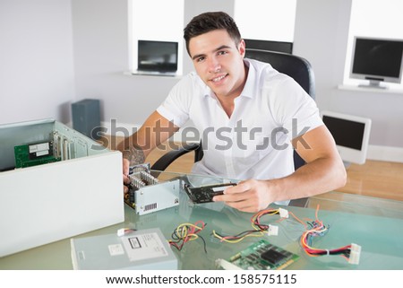 Attractive smiling computer engineer sitting at desk holding hardware in bright office