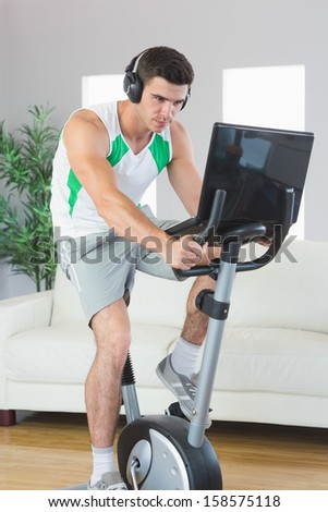 Determined handsome man training on exercise bike using laptop in bright living room