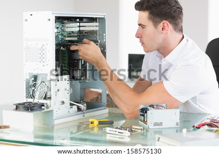 Handsome unsmiling computer engineer working at open computer in bright office