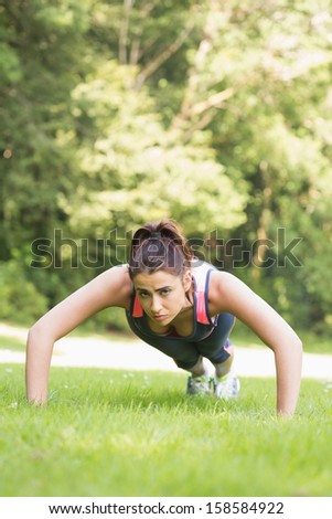 Focused fit woman doing plank position on the grass looking at camera