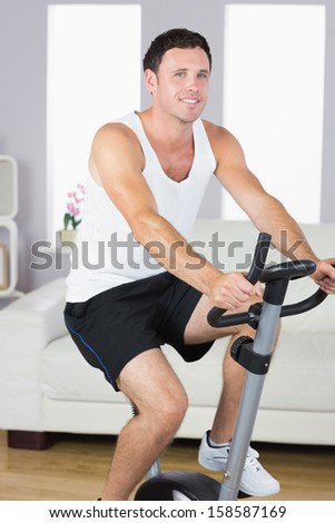 Smiling sporty man exercising on bike in bright living room