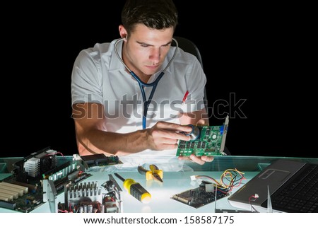 Attractive computer engineer examining hardware with stethoscope at his lit desk