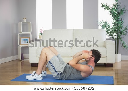 Handsome sporty man doing sit ups in bright living room