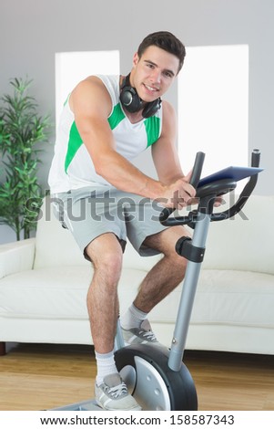 Content handsome man training on exercise bike using tablet in bright living room