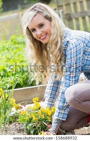 Blonde woman planting yellow flowers smiling at camera while working in the garden