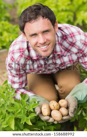 Young man holding some potatoes while crouching in his garden