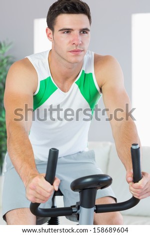 Unsmiling handsome man training on exercise bike in bright living room