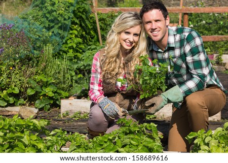 Smiling young couple crouching in their garden holding a plant smiling at camera