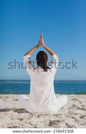 Brunette woman sitting back to camera practicing yoga at beach on a sunny day