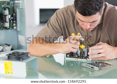 Handsome frowning computer engineer repairing hardware with pliers in bright office