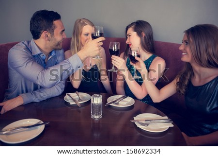 Smiling friends clinking wine glasses and chatting in a restaurant