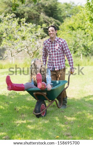 Man pushing his girlfriend in a wheelbarrow in a sunny garden