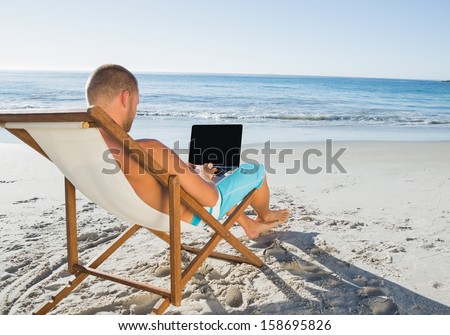 Relaxed handsome man working on his laptop on the beach