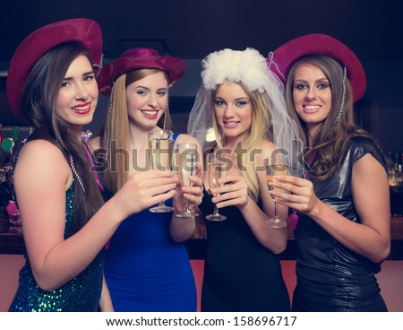 Attractive friends clinking champagne glasses at hen night looking at camera