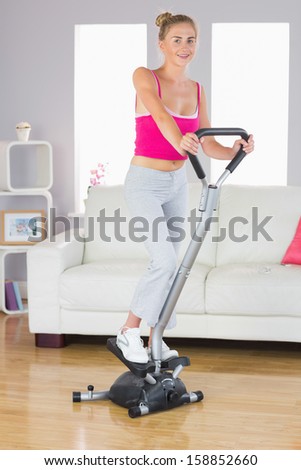 Sporty smiling blonde training on step machine in bright living room