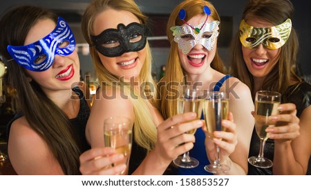 Smiling friends holding champagne glasses wearing masks looking at camera