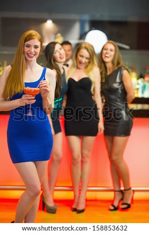Smiling woman standing in front of her friends holding cocktail  looking at camera