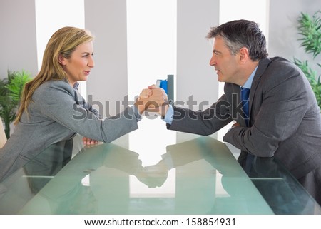 Two irritated mature businesspeople having an arm wrestling sitting around a table at office