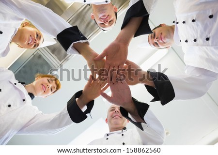 Chefs joining hands in a circle wearing uniforms in a kitchen
