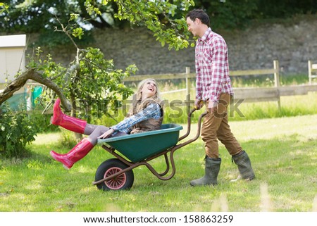 Handsome man pushing his laughing girlfriend in a wheelbarrow in a sunny garden