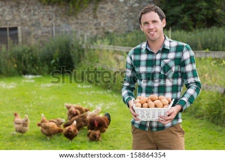 Proud young man holding a basket filled with eggs with chickens behind him