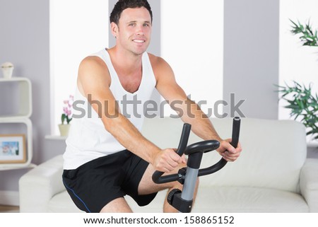 Cheerful sporty man exercising on bike in bright living room