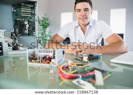 Attractive computer engineer sitting at desk smiling at camera in bright office