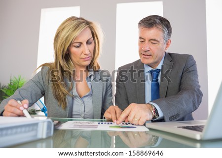 Two unsmiling mature business people pointing at a graphic at office