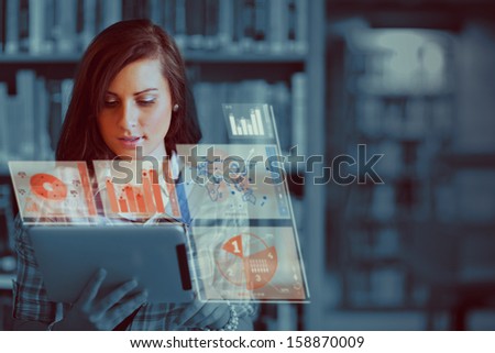 Pretty student working on her futuristic tablet computer in a library