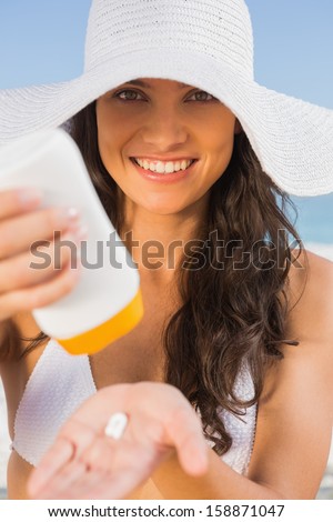 Smiling young brunette on the beach taking care of her body putting on sun cream
