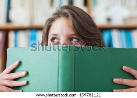 Close-up portrait of a female student holding book in front of her face in the library - stock photo