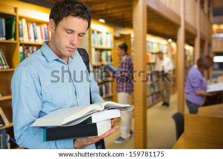 Serious mature student reading book with people in the background in the library