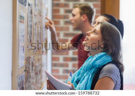 Casual Students Looking At Notice Board In College