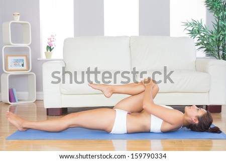 Young woman stretching her leg in yoga pose on exercise mat in her living room