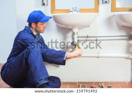 Attractive concentrating plumber repairing sink in public bathroom