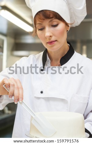 Pretty concentrating head chef finishing a cake with icing in professional kitchen