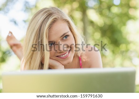 Happy day dreaming woman lying in front of her notebook on a lawn
