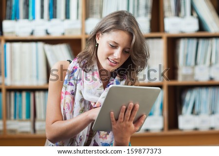 Female student using tablet PC against bookshelf in the library