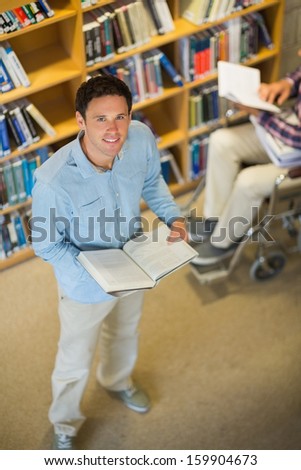 High angle view of a man by disabled student in wheelchair against bookshelf in the library