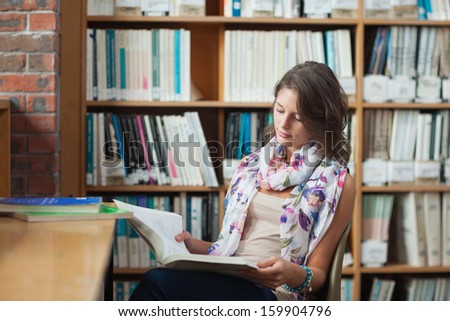 Female student sitting on chair and reading a book in the library