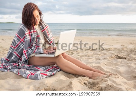 Young woman covered with blanket using laptop at the beach