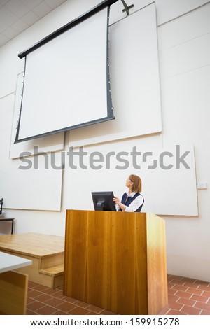 Elegant female teacher with computer and projection screen in the lecture hall