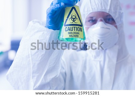 Close-up of a scientist in protective suit with hazardous blue chemical in flask at the laboratory
