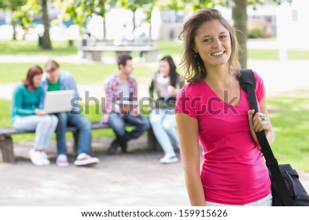 Portrait of college girl smiling with blurred students sitting in the park
