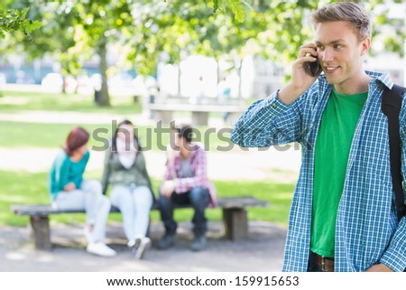 College boy using mobile phone with blurred students sitting in the park