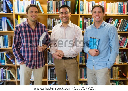 Portrait of three smiling mature students standing together in the library