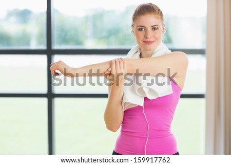 Portrait of a fit woman with towel around neck stretching hand in fitness studio